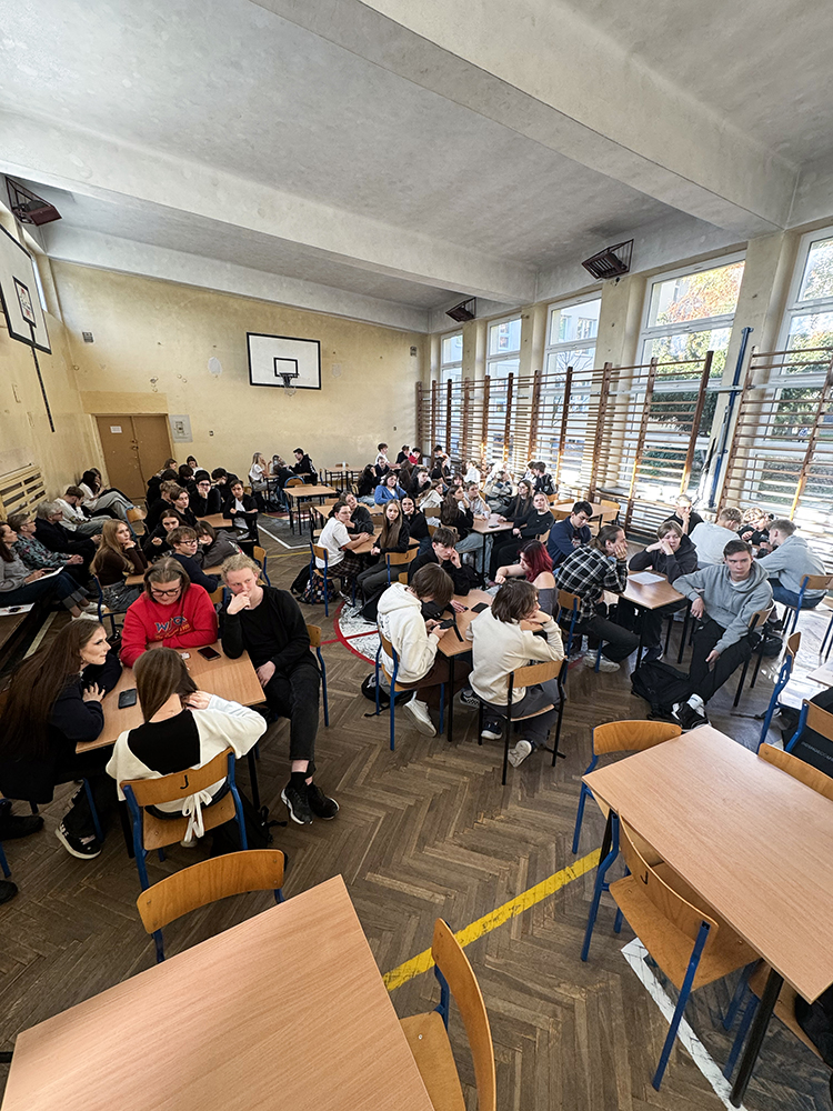 Uczniowie siedzący przy stolikach na sali gimnastycznej